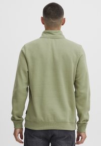 Sudadera de forro polar verde claro con cuello alto y puños acanalados. La tela es suave y texturizada, con un diseño sutil.