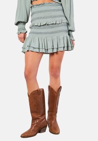 Ljusgrön, volangig mini kjol med elastisk smockning, kombinerad med bruna läder cowboystövlar med detaljrika utskärningar och klack.