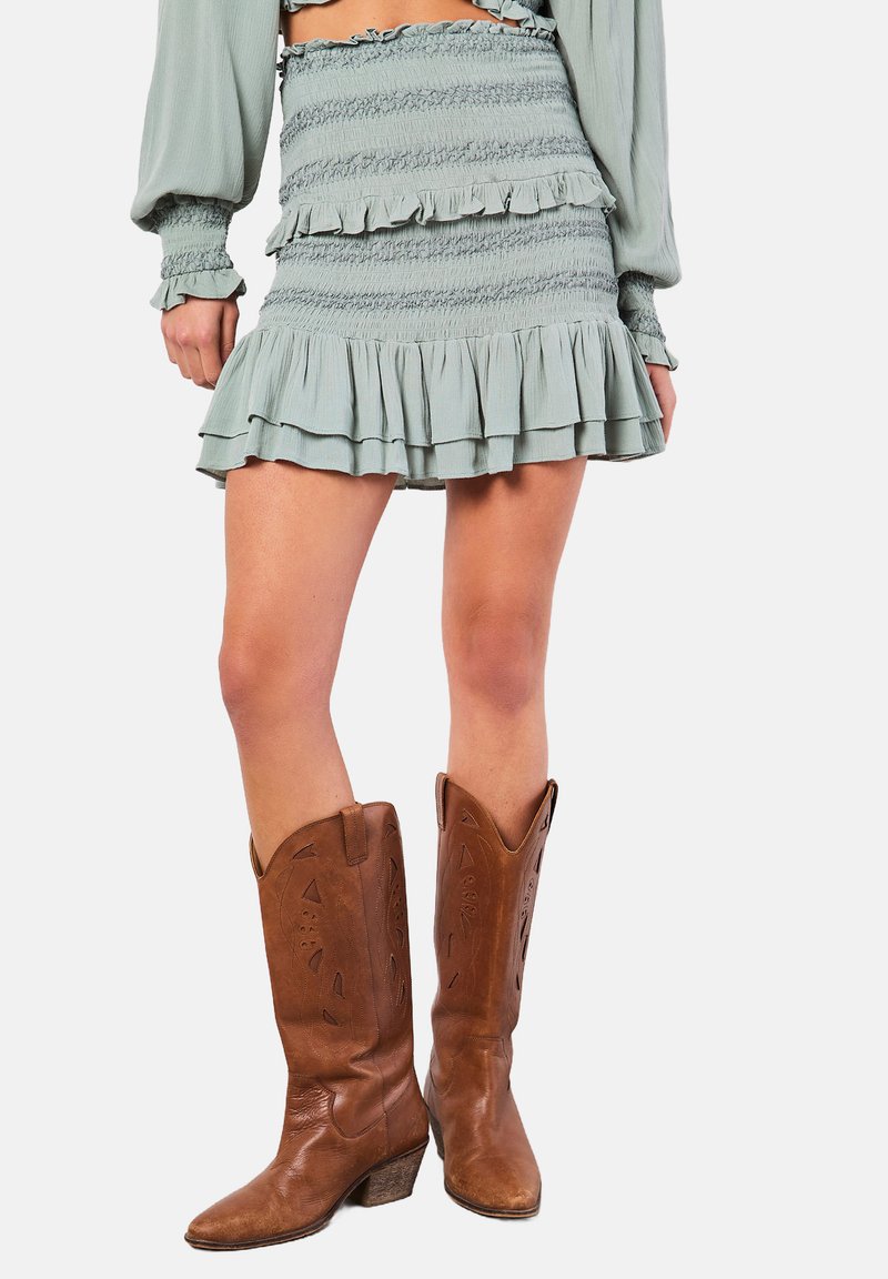 Ljusgrön, volangig mini kjol med elastisk smockning, kombinerad med bruna läder cowboystövlar med detaljrika utskärningar och klack.