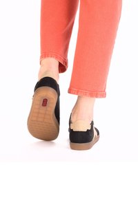 Black and tan slip-on shoes with a textured sole, featuring a small logo detail and a soft back with a slight heel.