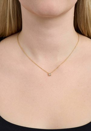 Kultainen ketjukaulakoru, jossa on pieni neliönmuotoinen timanttiripustin, puettu kaulaan paljaan ihon ja mustan topin päälle.
