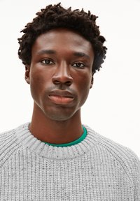 Grauer Strickpullover mit geripptem Ausschnitt, getragen über einem leuchtend grünen Hemd. Glatte Textur mit subtilen Variationen in der Garnstärke.