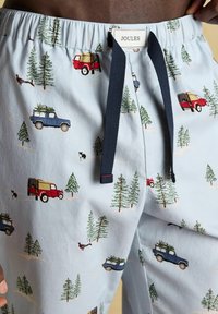 Gaiši zilas pidžamas bikses ar sarkano un zilo kravas automašīnu, zaļo koku un suņa motīviem. Ar elastīgu jostasvietu un tumši zilu auklu.