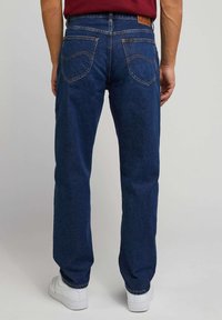 Menns blå denim jeans med rett ben-design, synlige sømmer og to baklommer. Brukt med hvite sneakers.