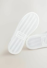 Soli de sneaker albe cu un model de șanțuri în zigzag și logo-ul "NEXT" embosat pe mijloc. Textură netedă și formă rotundă.