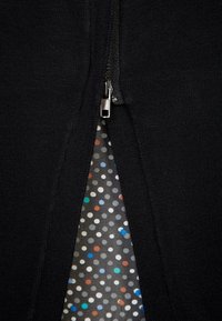 Černý oděv na zip s texturovanou vnější vrstvou a vnitřní podšívkou s puntíkovaným vzorem v různých barvách na tmavém pozadí.