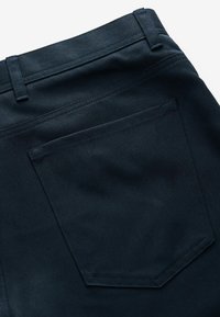 Dark blue denim trousers feature a smooth texture, a waistband with belt loops, and a single rear pocket with double-stitched accents.