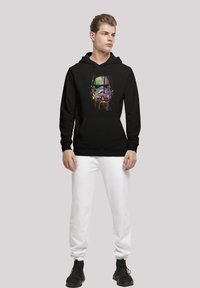Svart hoodie med en färgglad, sprutad stormtrooper-grafik. Kombinerad med vita sweatpants och svarta skor. Avslappnad design och passform.