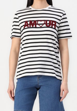 Femme portant une chemise à manches courtes rayée noir et blanc avec "AMOUR" et un cœur rouge au centre, associée à un jean bleu.