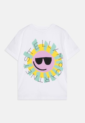 Biały t-shirt z kolorowym wzorem słońca, które ma na sobie czarne okulary przeciwsłoneczne i uśmiech, otoczony abstrakcyjnymi zielonymi i żółtymi kształtami.