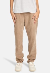 Hellbraune Cordhosen mit geradem Bein und strukturierter Oberfläche, kombiniert mit weißen Sneakers. Einfarbiges graues T-Shirt ist oben sichtbar.