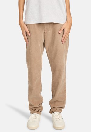 Light brown corduroy pants with straight legs and a textured finish, paired with white sneakers. Plain grey T-shirt visible at the top.