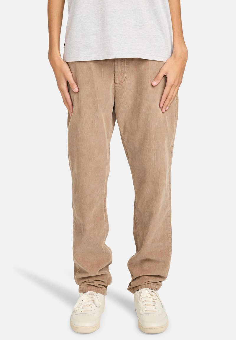 Hellbraune Cordhosen mit geradem Bein und strukturierter Oberfläche, kombiniert mit weißen Sneakers. Einfarbiges graues T-Shirt ist oben sichtbar.