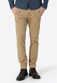 Beige Baumwoll-Chinos mit geradem Schnitt, ausgestattet mit Seitentaschen und einem sauberen Finish, kombiniert mit braunen Schnürstiefeln.