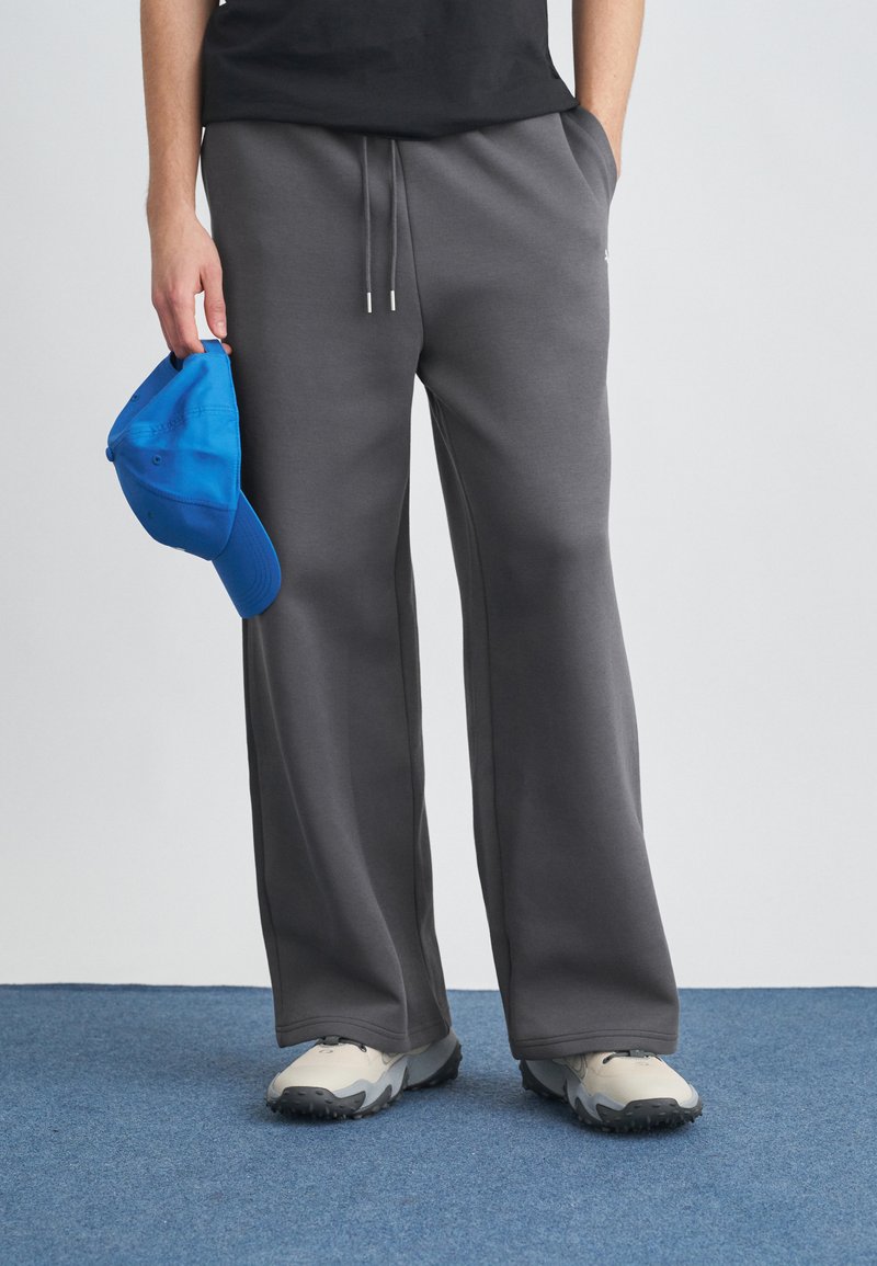 Szare spodnie dresowe o luźnym kroju z sznurkiem, zestawione z niebieską czapką. Materiał wydaje się miękki o gładkiej fakturze, bez widocznych wzorów.