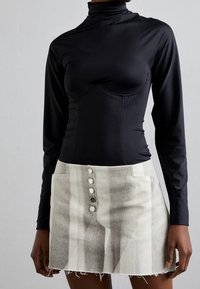 Svart långärmad bodysuit med hög krage och åtsittande design; kombinerad med en ljusgrå minikjol med vertikala ränder och knappar som detaljer.