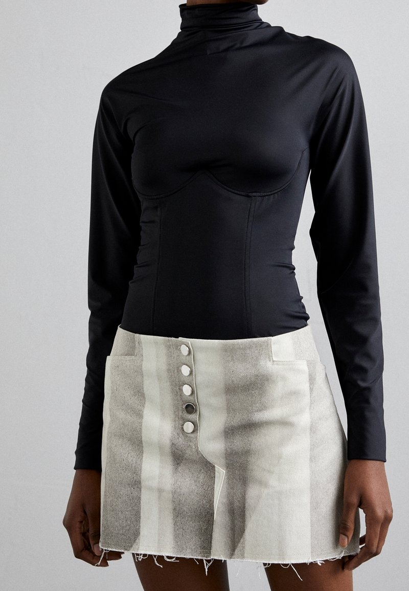 Svart långärmad bodysuit med hög krage och åtsittande design; kombinerad med en ljusgrå minikjol med vertikala ränder och knappar som detaljer.