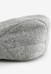 Grijze wollen baret met een afgeronde top, gestructureerd oppervlak en gestikte details langs de naden. De stof lijkt zacht en warm.
