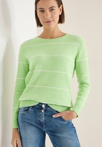 Pull en maille côtelée vert clair avec des rayures horizontales blanches, col rond et manches longues, associé à un jean en denim bleu.