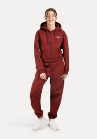Maroonowy hoodie oraz dopasowane dresy wykonane z miękkiego materiału. Hoodie ma kieszeń z przodu oraz sznurki do ściągania, a dresy mają elastyczne mankiety.