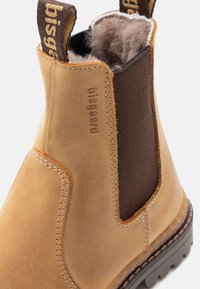 Bottines en cuir tan avec des panneaux élastiques marron, des coutures marron et une semelle en caoutchouc texturé. Elles disposent d'une doublure intérieure douce.
