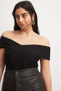 Top nero off-shoulder con texture a coste e design aderente, abbinato a pantaloni in pelle nera a vita alta con chiusura a bottoni.