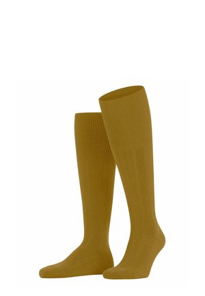Chaussettes jaunes moutarde montant jusqu'aux genoux, fabriquées en matériau côtelé, avec une texture lisse et une coupe ajustée qui épouse la forme de la jambe.