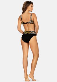 Kostium kąpielowy w zestawie z czarnym dołem i topem w wielokolorowy wzór liści. Posiada grube ramiączka oraz wysoki stan, co zapewnia dodatkowe krycie.