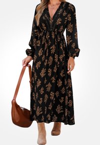 Černé květinové maxi šaty s dlouhými rukávy, s véčkovým výstřihem a propracovanými hnědými květinovými vzory. V páru s hnědou kabelkou přes rameno a béžovými kotníkovými botami.