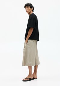 T-shirt noir à manches courtes avec une coupe décontractée, associé à un bermuda beige jusqu'aux genoux en tissu lisse. Des sandales noires complètent le look.