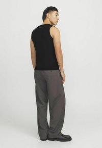 Sort ribbet tanktop parret med løstsiddende grå bukser. Stoffet har en glat tekstur, og outfittet inkluderer sort fodtøj.