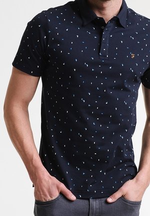 Marineblå polo-shirt med prikmønstre i lyst blå og hvid, lavet af bomuldsstof, med klassisk krave og korte ærmer.