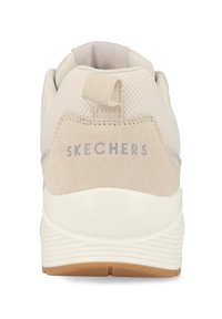 Zapato deportivo beige con parte superior de malla texturizada y tacón de ante. Cuenta con una tira en el talón, el logotipo "SKECHERS" y una entresuela blanca acolchada.