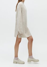 Robe pull tricotée en beige clair avec des manches amples et des fentes sur les côtés. Assortie à des mocassins épais beiges et des chaussettes côtelées roses.