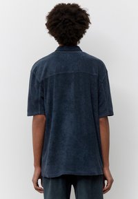 Kortärmad marinblå frottéskjorta med krage, avslappnad passform och synliga söm detaljer, visad bakifrån.