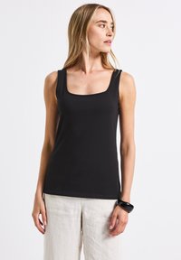 Top nero aderente con scollatura quadrata e spalline larghe. Realizzato in un tessuto morbido, abbinato a pantaloni in lino di colore chiaro.