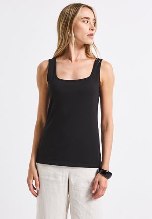 Black, fitted tank top with a square neckline and wide shoulder straps. Made from a smooth fabric, paired with light-colored linen pants.