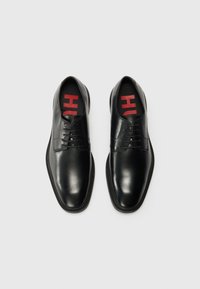 Zwarte leren dresschoenen met een gladde afwerking, vetersluiting en rood logo op de binnenkant van de zool. Ronde neus en platte zolen.