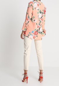 Blommig blus i persika med lös passform, långa ärmar med knytdetaljer, matchad med vita cropped jeans och röda högklackade sandaler.