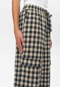 Pantalons en plaid beige et marine avec une coupe décontractée, dotés d'une taille élastique, d'un cordon de serrage et de poches latérales. Tissu en coton texturé.