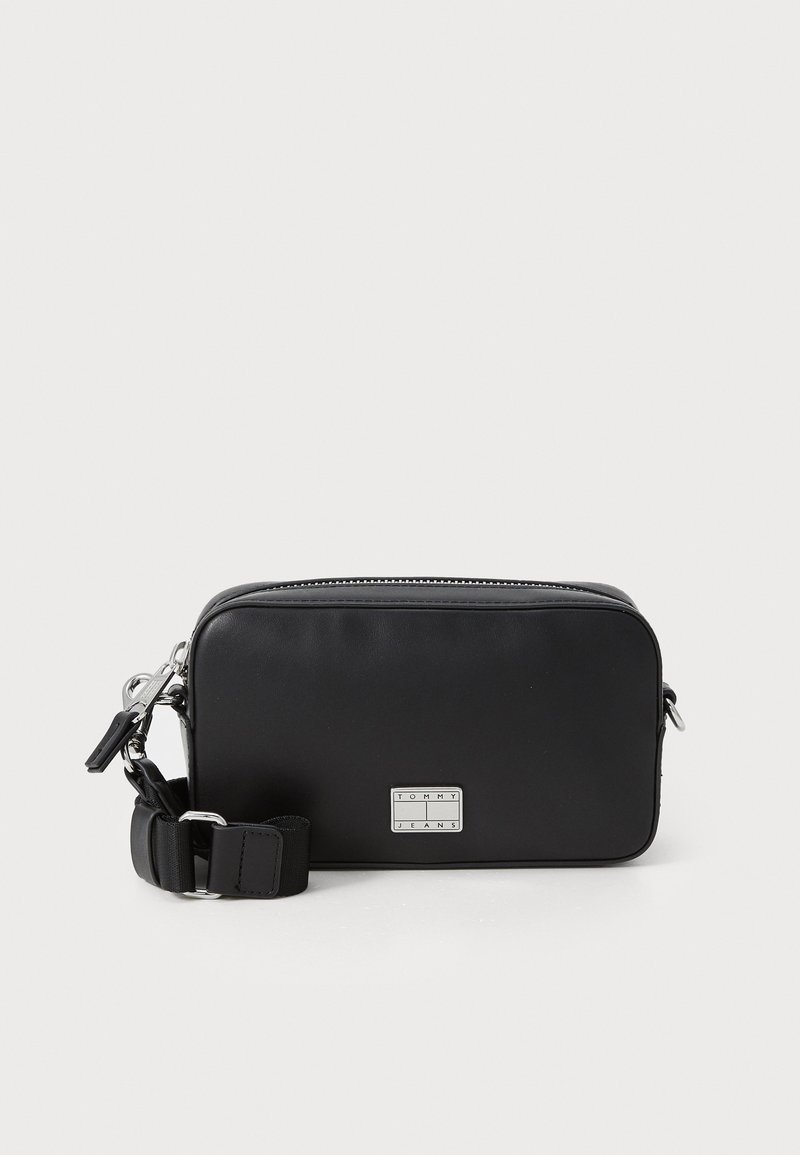 Svart syntetisk crossbody-väska med rektangulär form, dragkedjestängning, justerbar rem och metall-logoplåt på framsidan. Slät textur.
