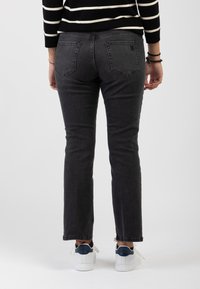 Jeans in denim grigio con una vestibilità slim e una leggera svasatura all'orlo, con tasche posteriori e un discreto dettaglio di cucitura, abbinati a sneakers bianche.