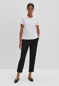 Weißes kurzärmliges T-Shirt, kombiniert mit schwarzen maßgeschneiderten Hosen. Das Outfit zeichnet sich durch ein einfaches Design und eine glatte Stofftextur aus, ergänzt durch schwarze Ballerinas.