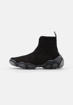 Zapatilla tipo calcetín de caña alta en negro con parte superior de punto perforado y suela texturizada en negro y gris sobre un fondo blanco.
