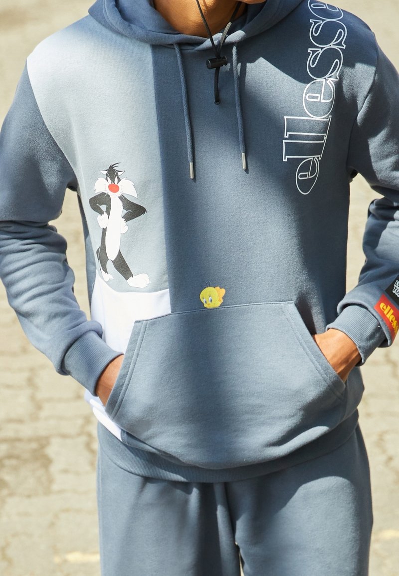 Felpa con cappuccio caratterizzata da blocchi di colore grigio e bianco. Presenta grafiche di Sylvester il gatto e Tweety Bird. Materiale morbido, tasca frontale, polsini a coste.