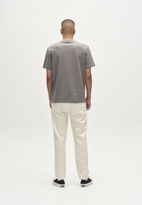 Szürke pamut rövid ujjú póló, krémszínű melegítőnadrággal párosítva. Fekete sportcipők kontrasztot adnak az öltözékhez.