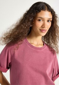 Kortärmad T-shirt i dammig ros med rund halsringning, mjukt tyg, avslappnad passform och minimal sömdetalj.