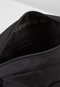 Borsa in tessuto nero con chiusura a zip. Interno foderato in nero, presenta una piccola tasca con zip e un'etichetta testurizzata. Design pulito e minimalista.