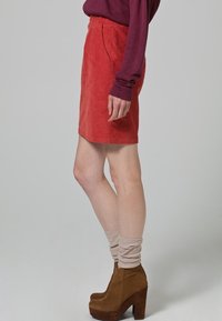 Mini falda de terciopelo rojo con una textura suave, que presenta bolsillos laterales. Combinada con botines de plataforma marrones y calcetines beige de caída.