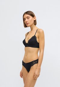 Crni komplet donjeg rublja koji se sastoji od braletice s čipkom i odgovarajućih tanga. Dizajn uključuje fine cvjetne uzorke i tanke podesive trake.